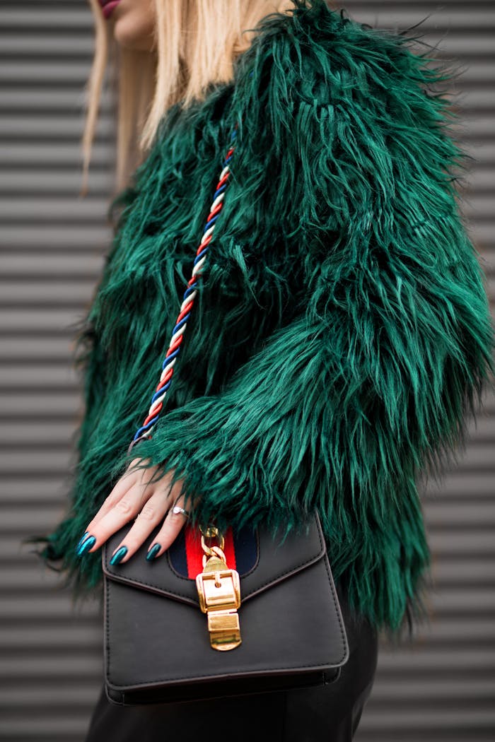 menu-12 Stylish woman in a green faux fur jacket holding a fashionable handbag outdoors.