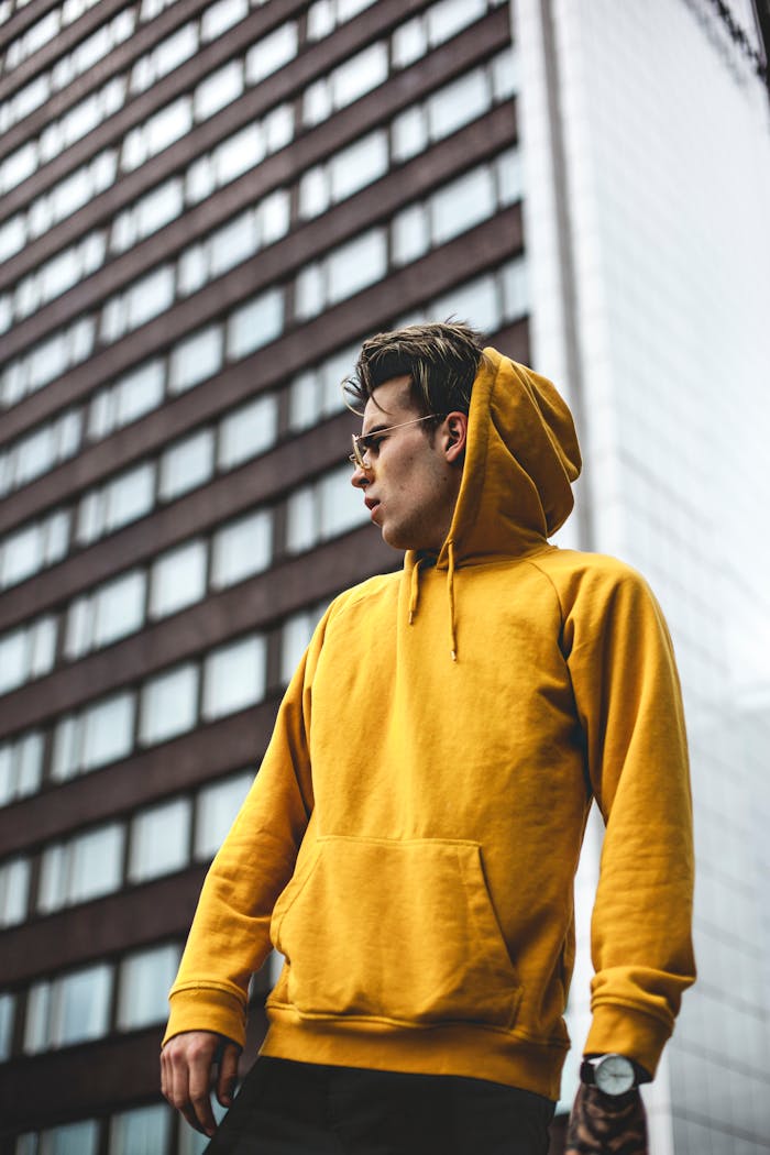 menu-02 Stylish man poses in yellow hoodie against urban building backdrop.