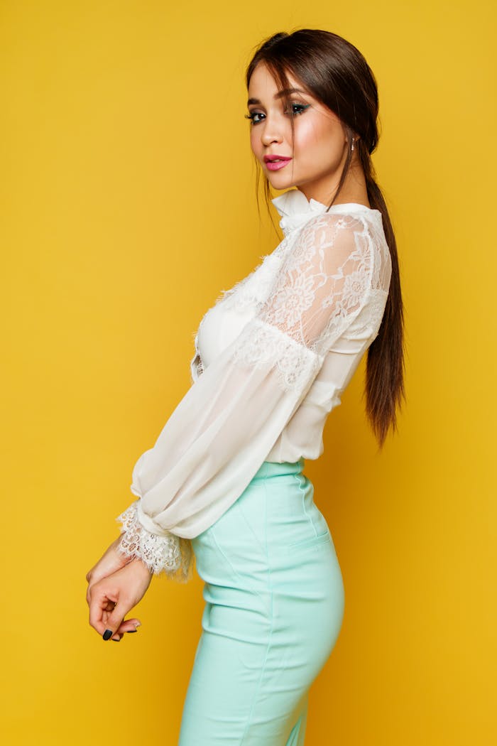 Fashionable woman in a white lace top and mint skirt posing against a vibrant yellow backdrop.