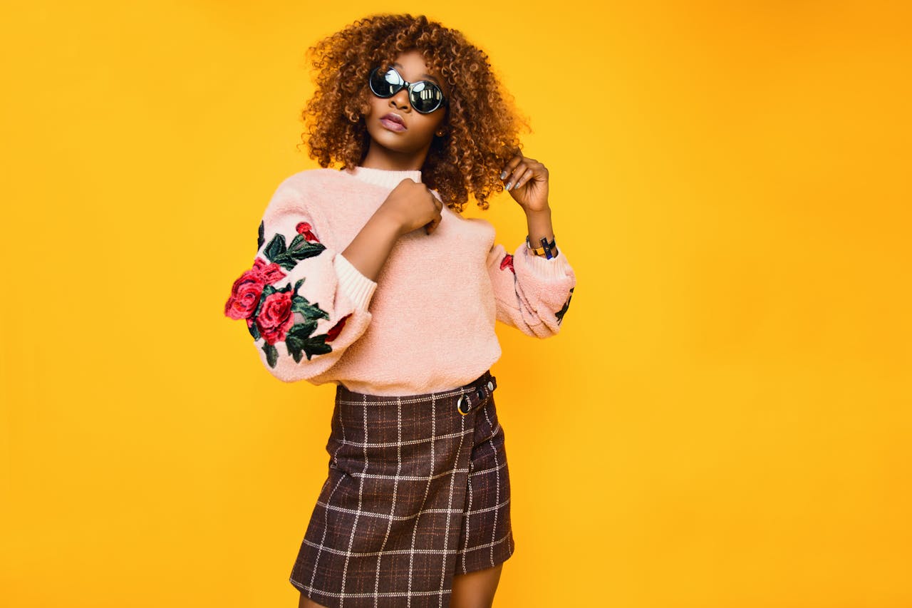 about-03 Chic woman with afro hair in a floral sweater and plaid skirt posing confidently.