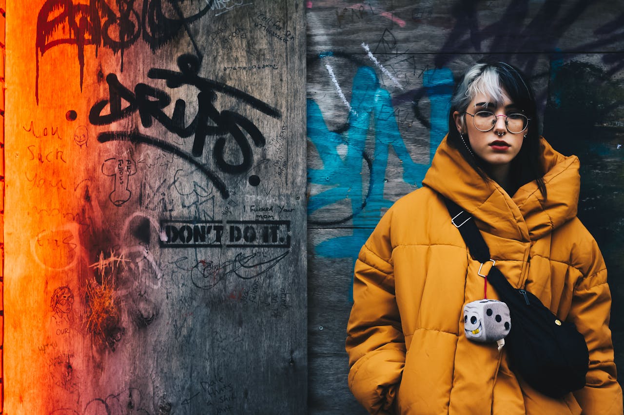 menu-06 Young woman in yellow winter jacket against vibrant graffiti wall, conveying urban street style.